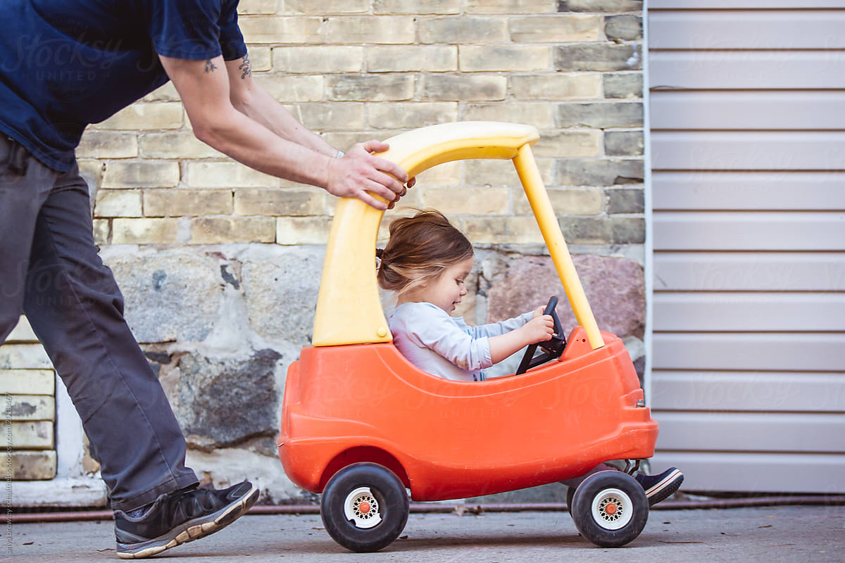 Toddler girl being pushed by her daddy in a toy car