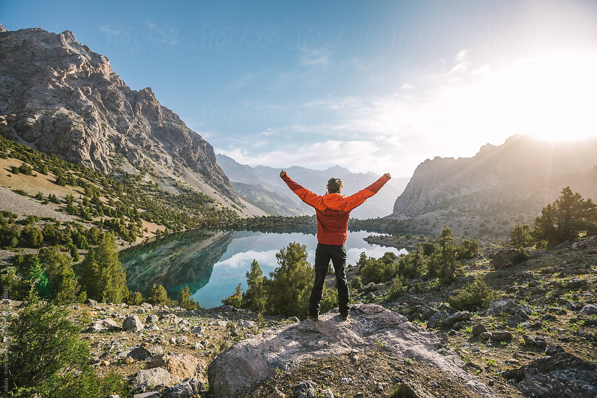 hiker in red jacket raise his hands at a beautiful mountain lake at sunrise