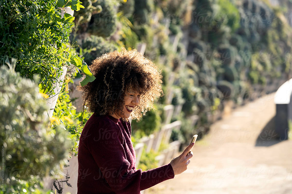Delighted woman with Afro hair using smartphone