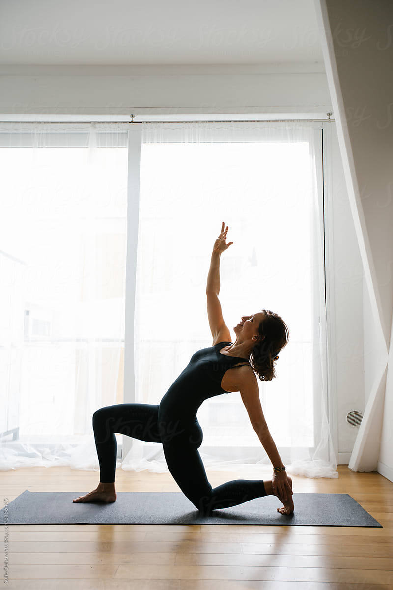 Barefooted flexible woman stretching body in standing bow pose while practicing yoga at home