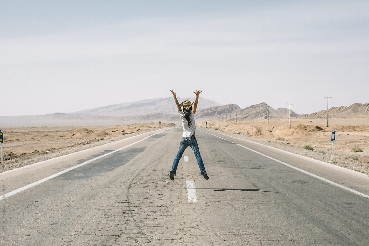 beautiful woman with hat jumping on a road in the desert