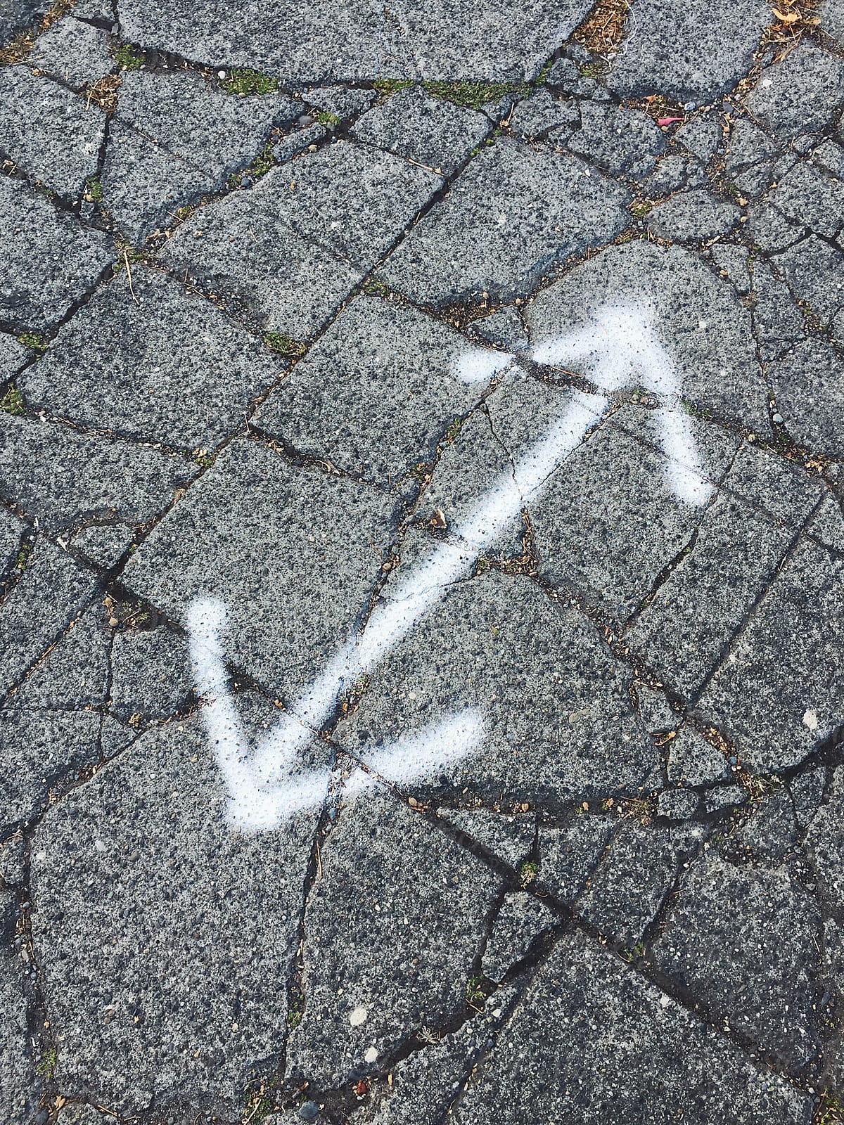 Spray painted double arrow sign on worn and cracked sidewalk