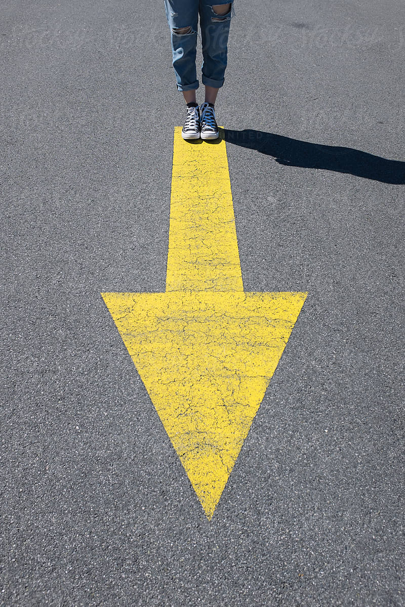 Girl standing on large yellow arrow on road