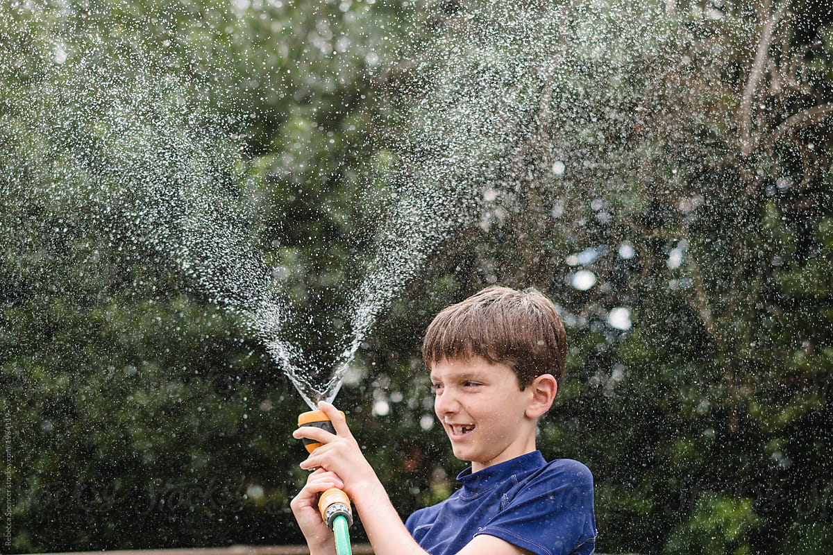 Happy child plays with a water hose in the garden