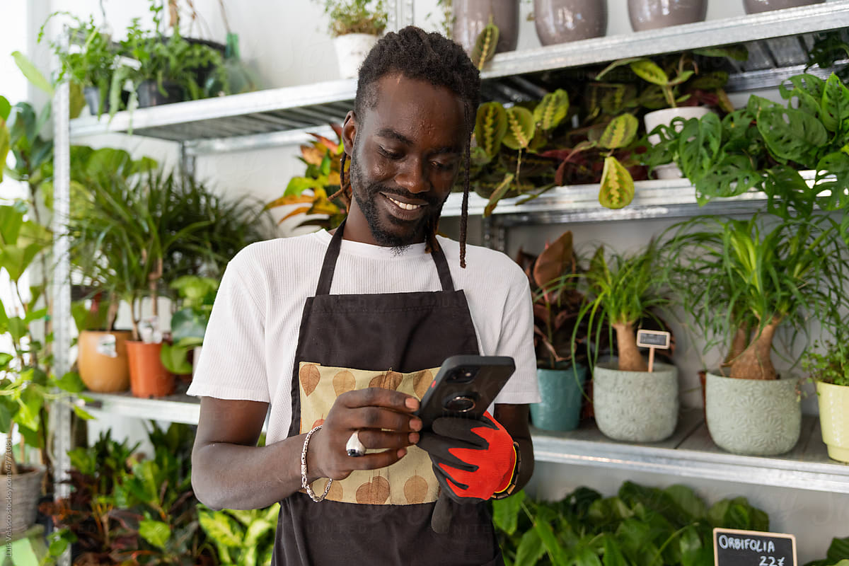 Black Man Using The Phone Working In A Plants Store.