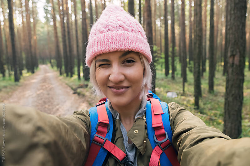 Girl in pink hat taking selfie against of forest road