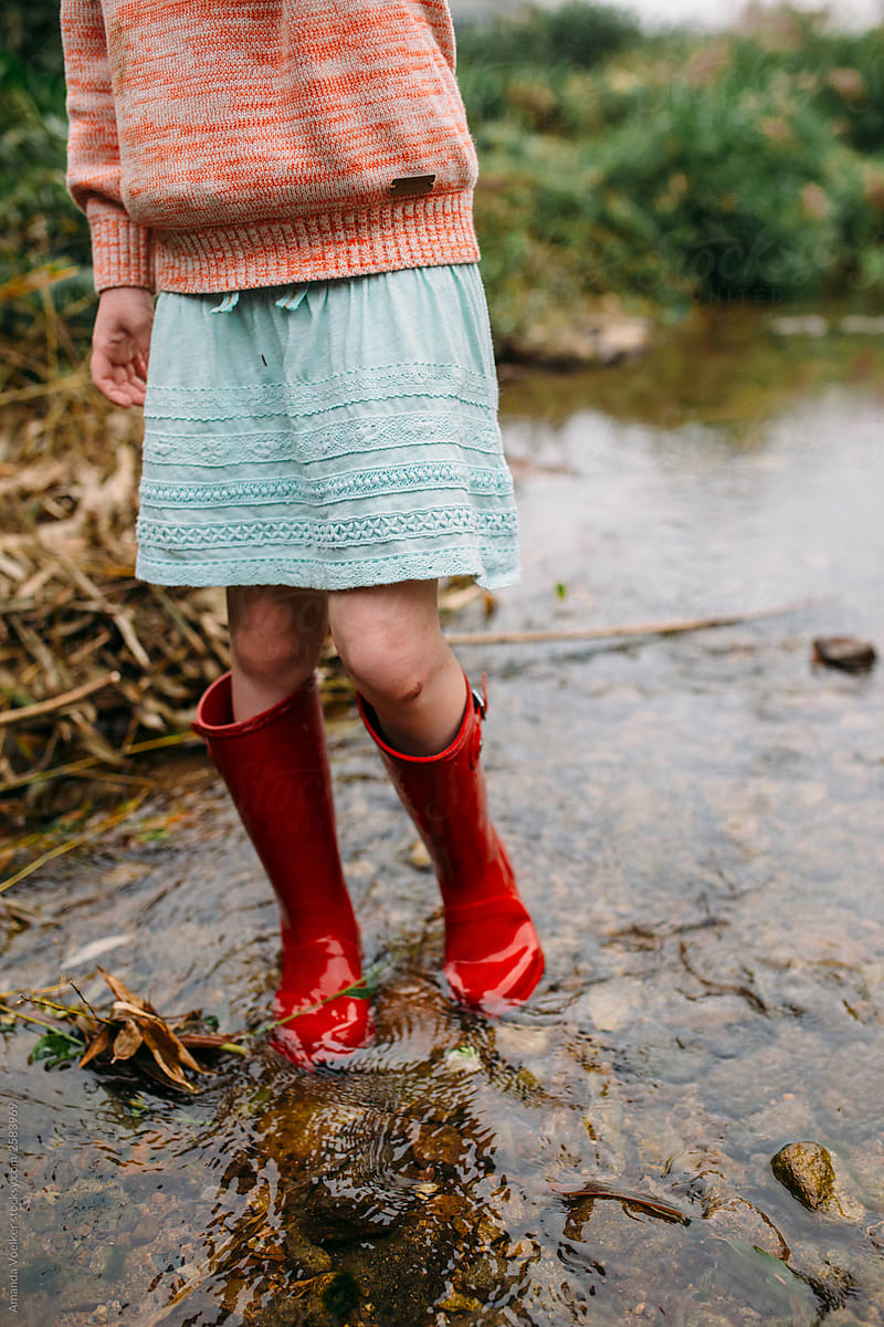 A little girl with skinned knees walks through a stream