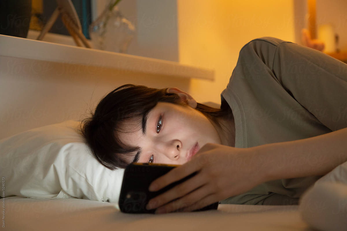 Asian female lying in bed browsing cellphone