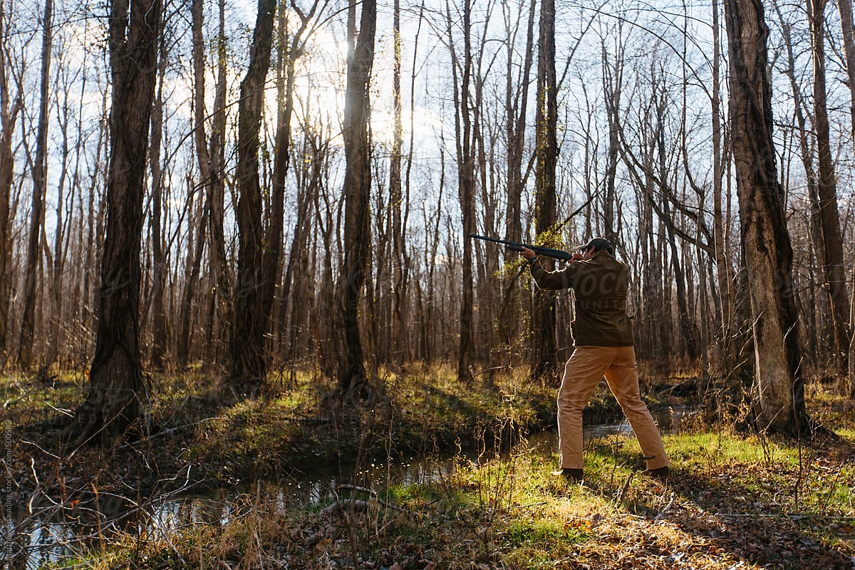 Man pointing and aiming gun in woods while hunting outdoors