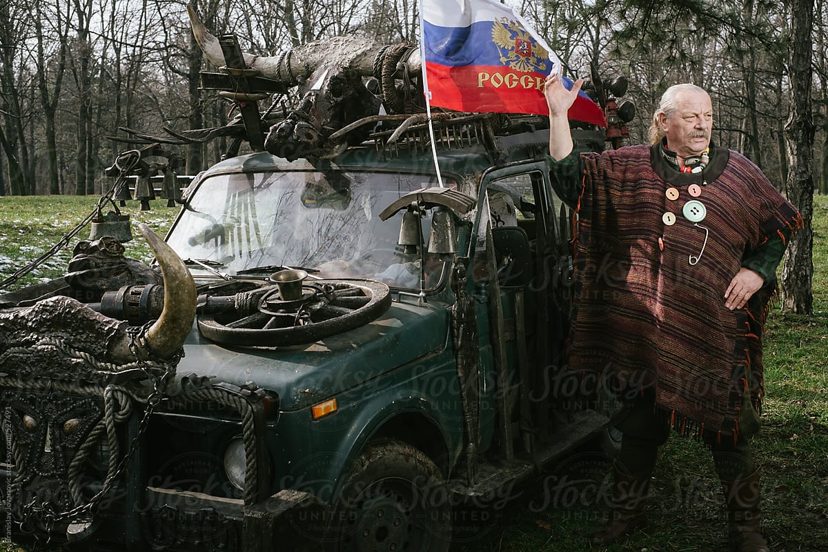 Eccentric old man standing beside his unique off-road vehicle with russian flag