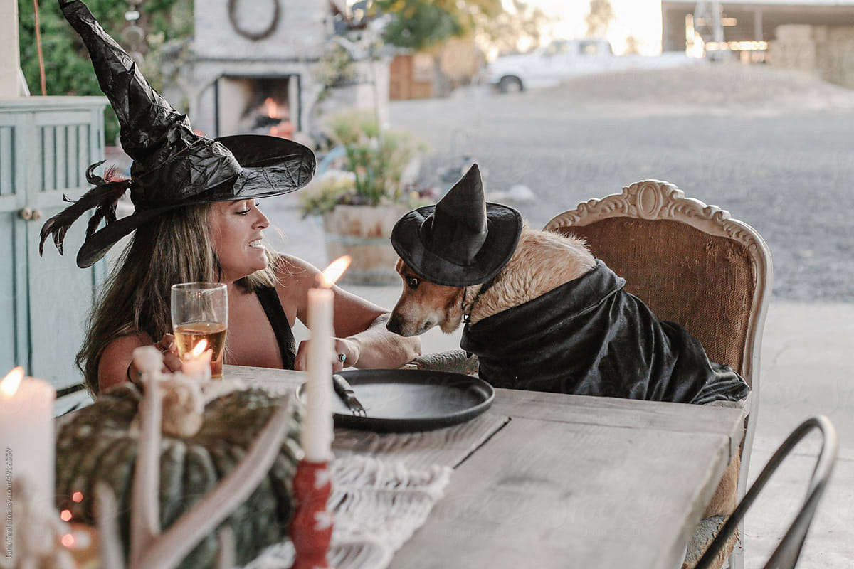 woman dressed as witch talks to dog dressed as witch sitting at table