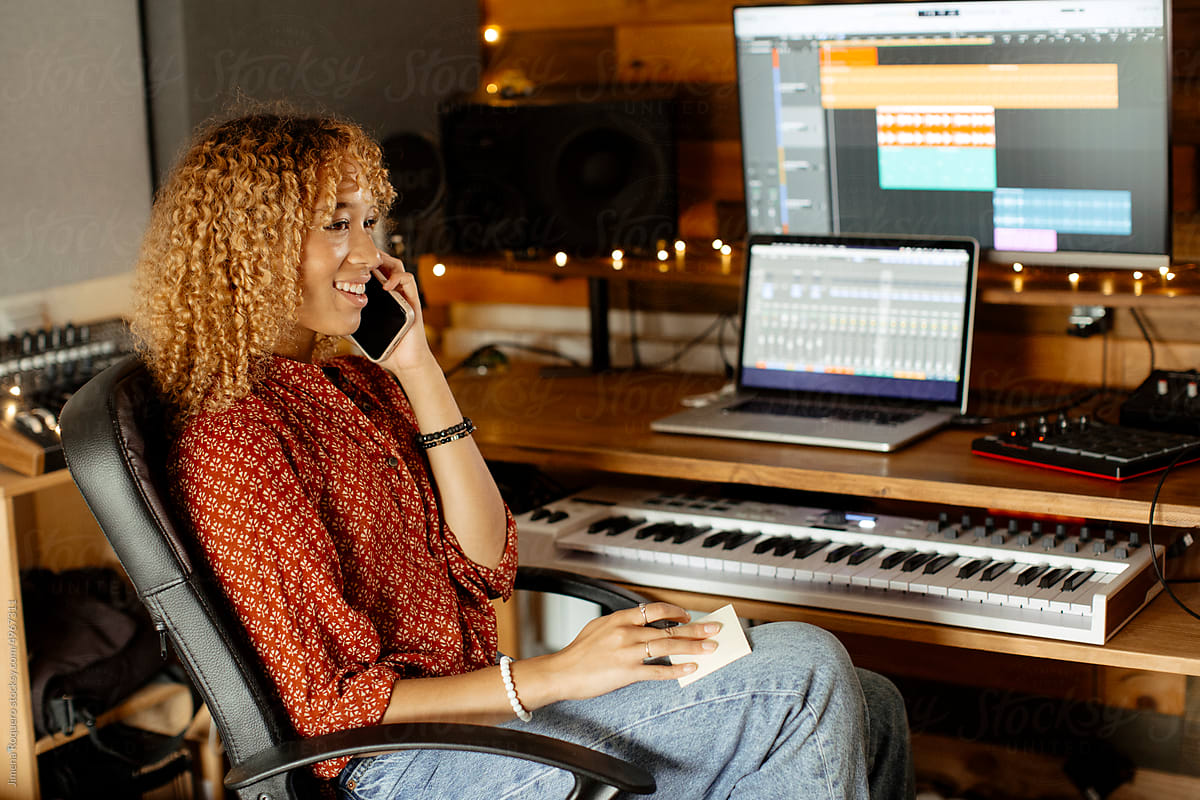 Audio producer at home studio talking on her cell phone on the desk