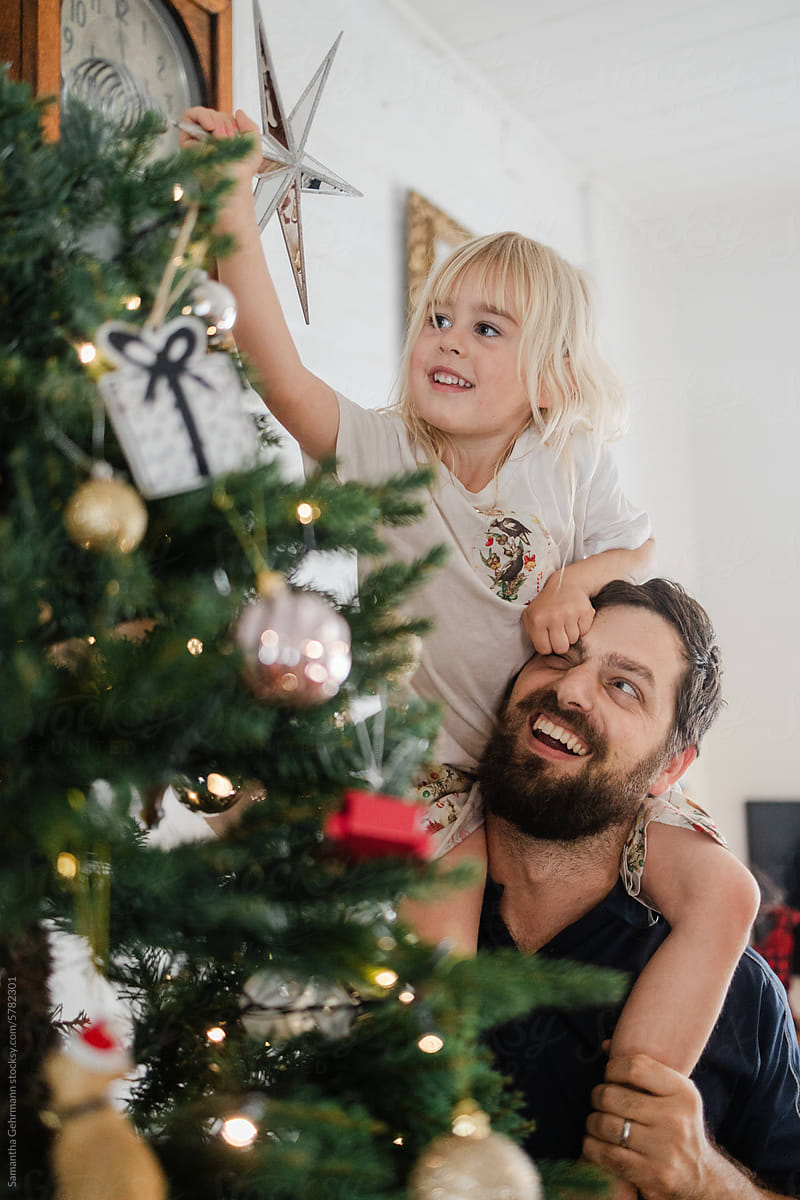 Little girl sits on fathers shoulders to place star on Christmas tree