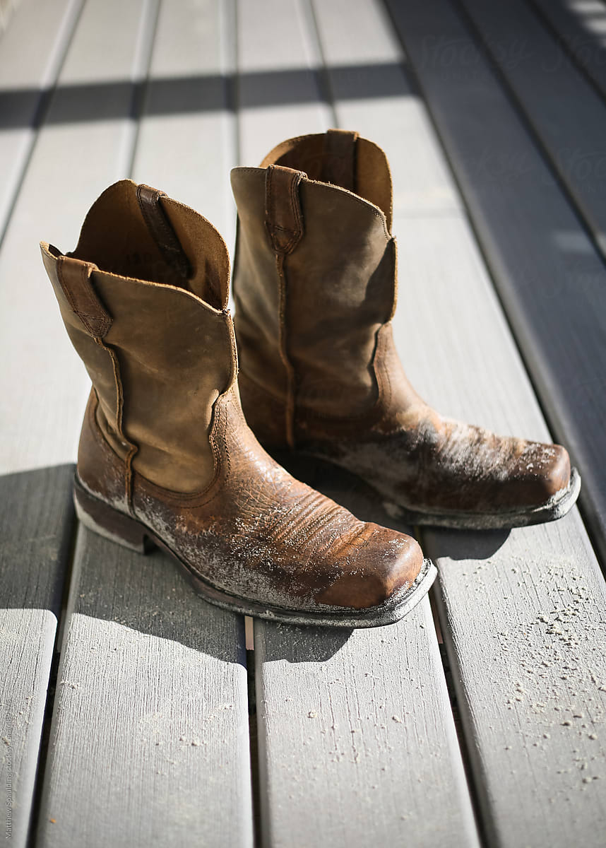 Empty sand covered leather cowboy boots on wood deck in sunlight