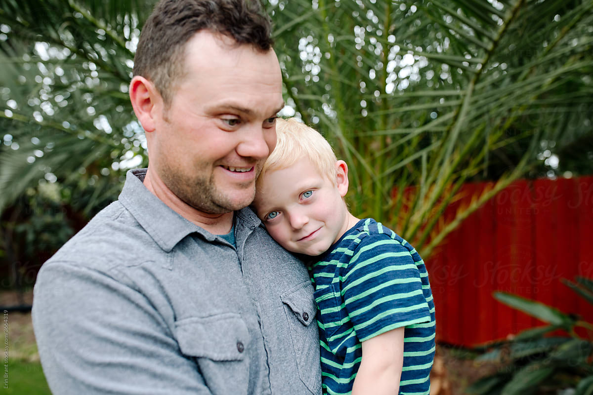 Happy dad holding young blue-eyed son in backyard
