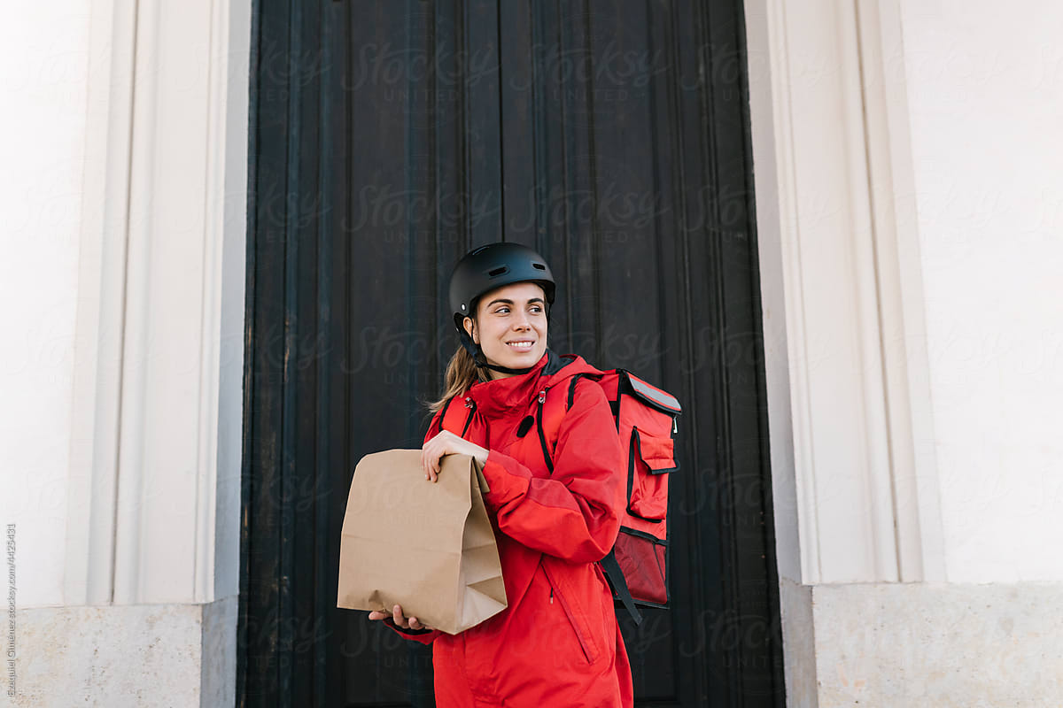 Smiling delivery lady with paper bag standing near door