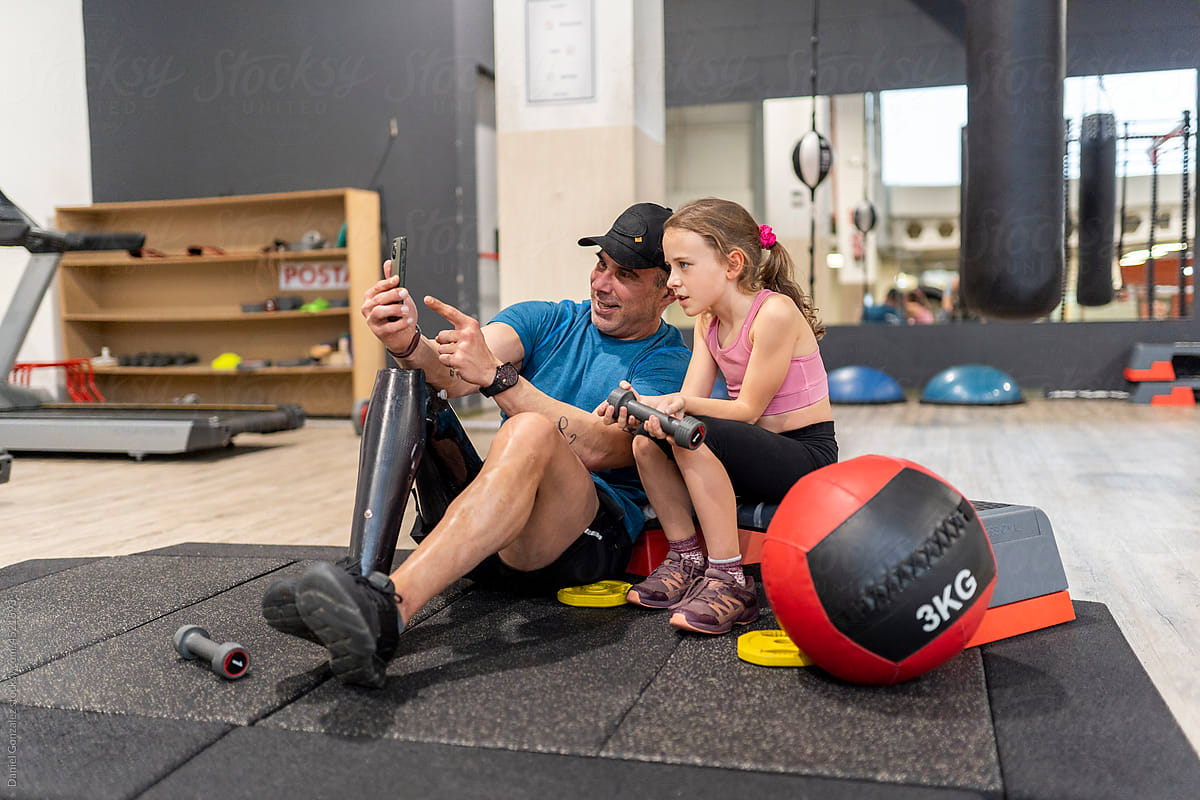 A disable man and his daughter at the gym with the phone