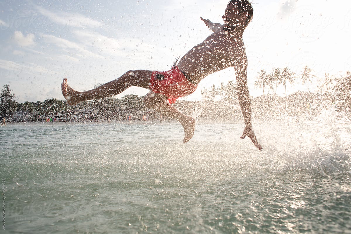 Happy man having fun in the ocean, captured jumping into the water
