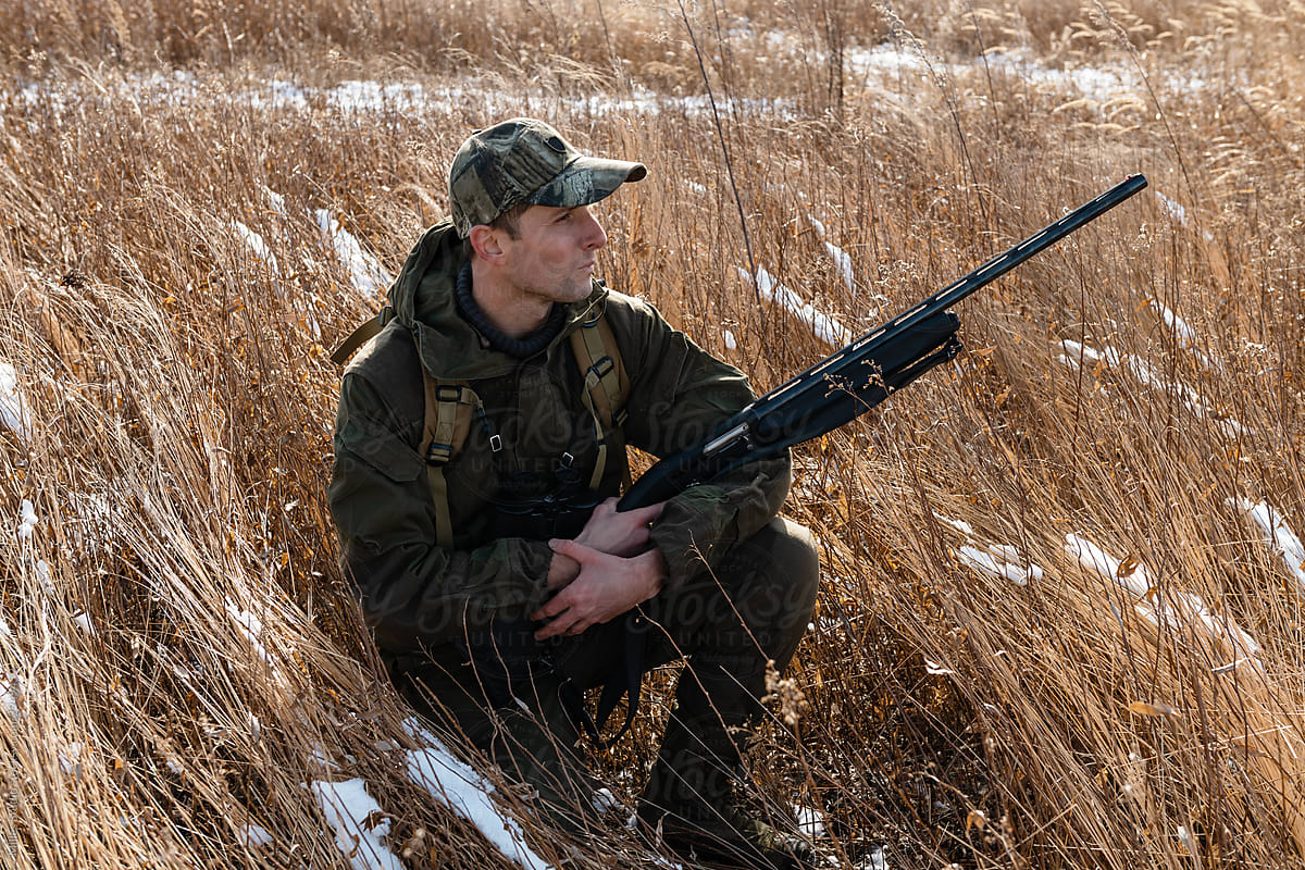 Man with hunting rifle resting in grassy field with snow