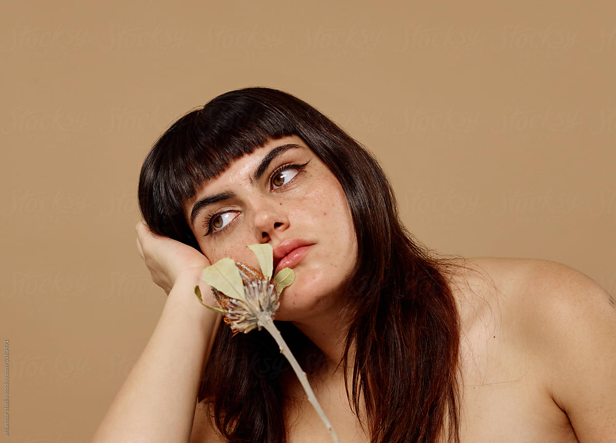 Woman with bored expression holding flower over beige background