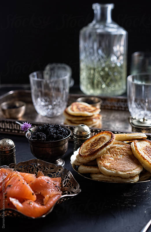 Blinis and ingredients for preparing them on a table,with drinks in the background.