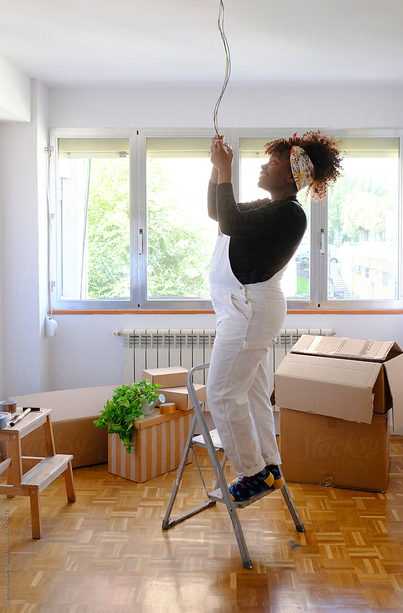 Pregnant woman in ladder fixing electric installation in new home
