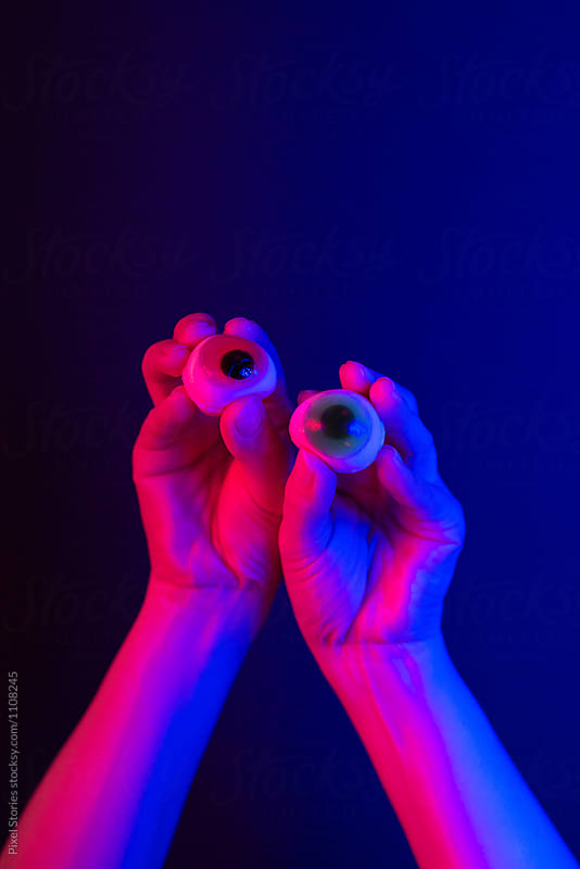 Hands holding two candy eyes over dark background
