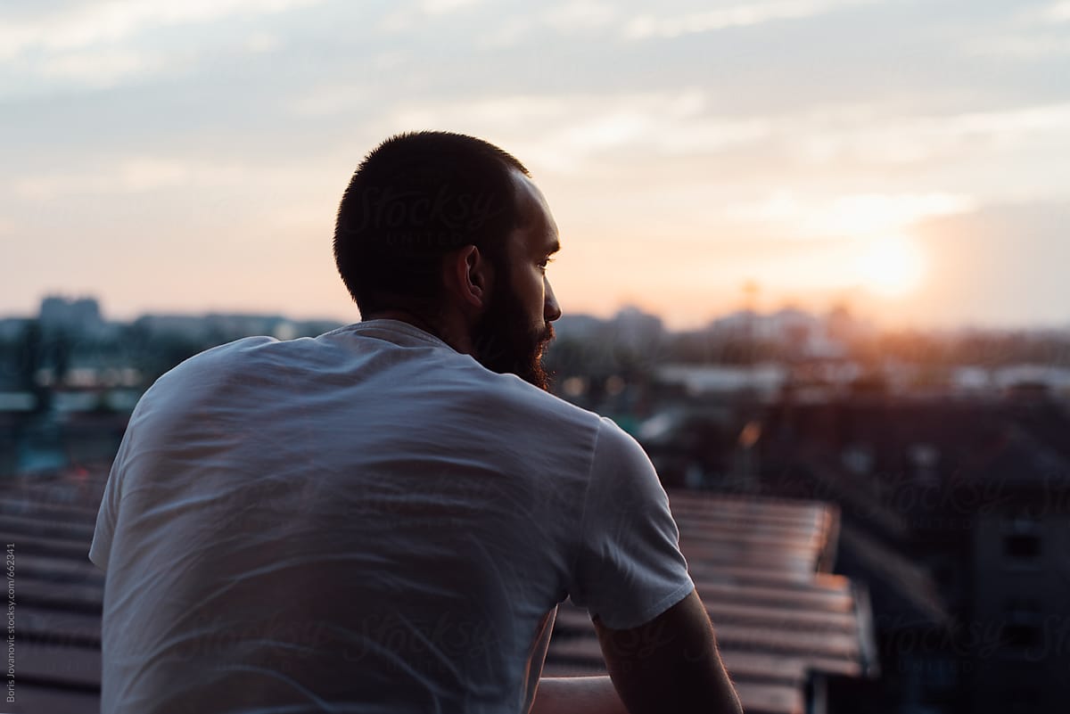 Back portrait of a man standing on terrace looking at the sunset