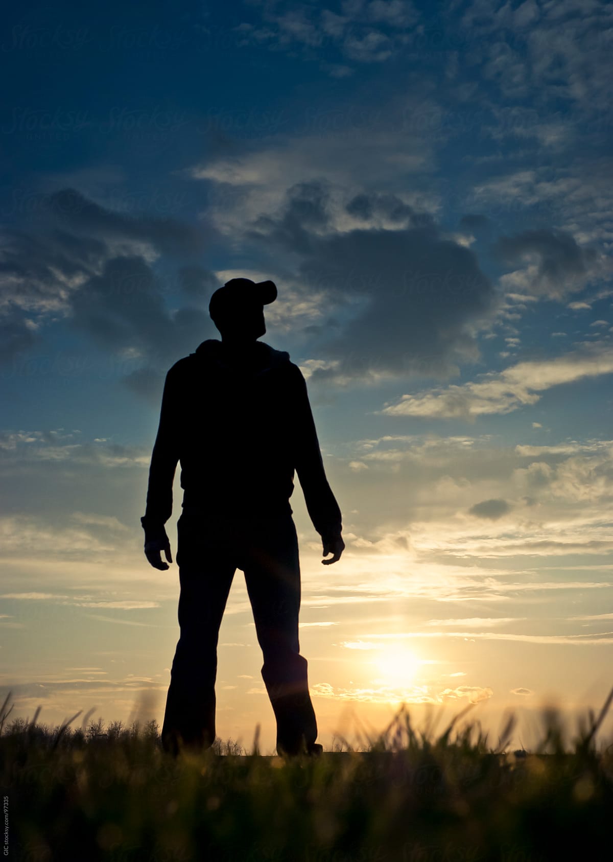 Silhouette Of Man Standing In A Field At Sunset By Stocksy