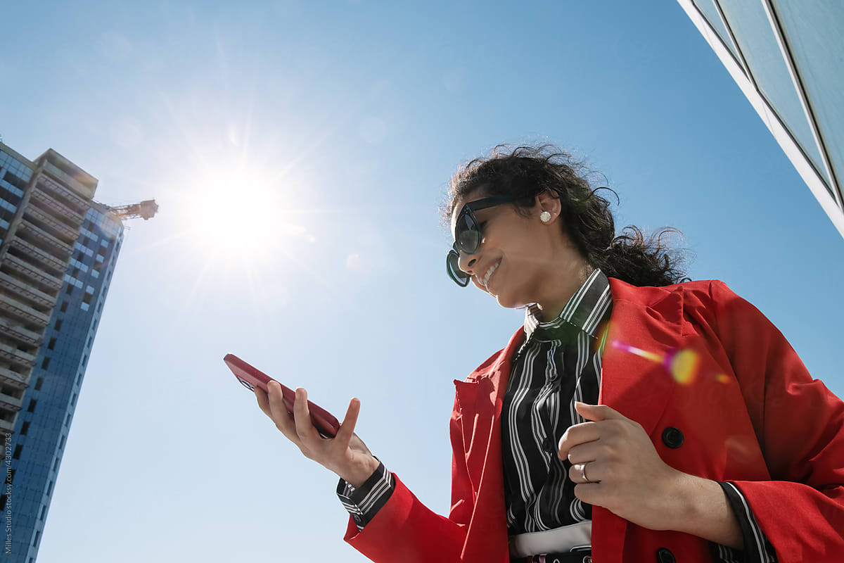 Cheerful businesswoman using cellphone against blue sky