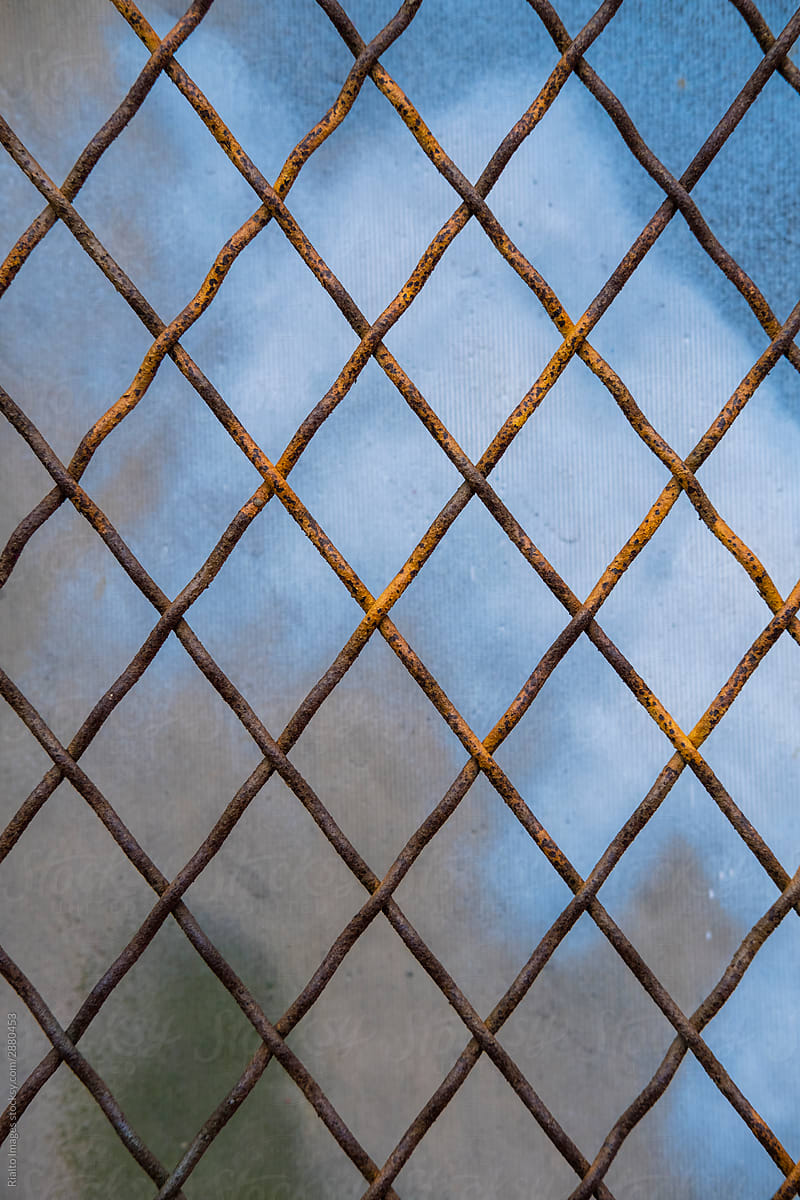 Detail of rusty chain-link fence, graffiti paint on wall in background