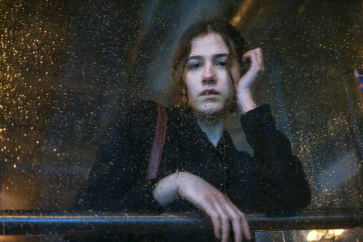 portrait of an attractive brunette girl looks into the camera through the wet glass during the rain