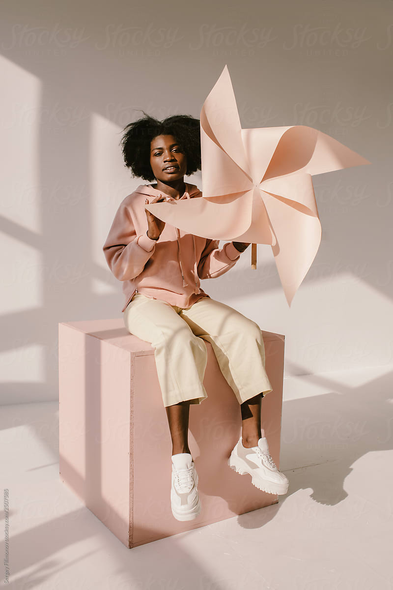 Cheerful black woman with pinwheel sitting on cube