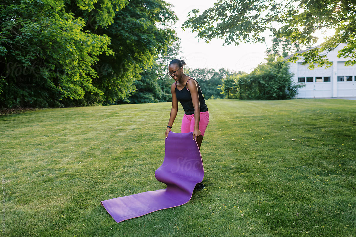 fit black girl with yoga mat outdoors on lawn at sunset