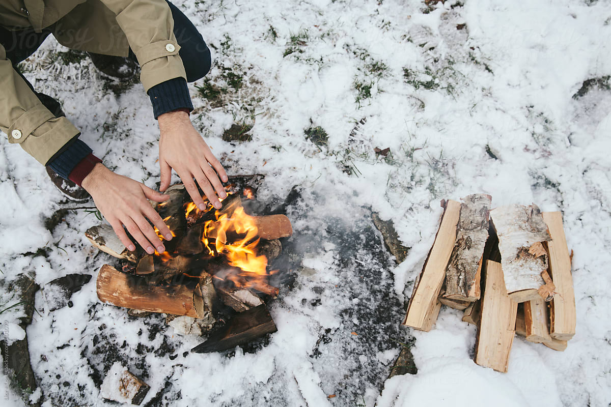 Man’s hands warming over a wood fire in the snow