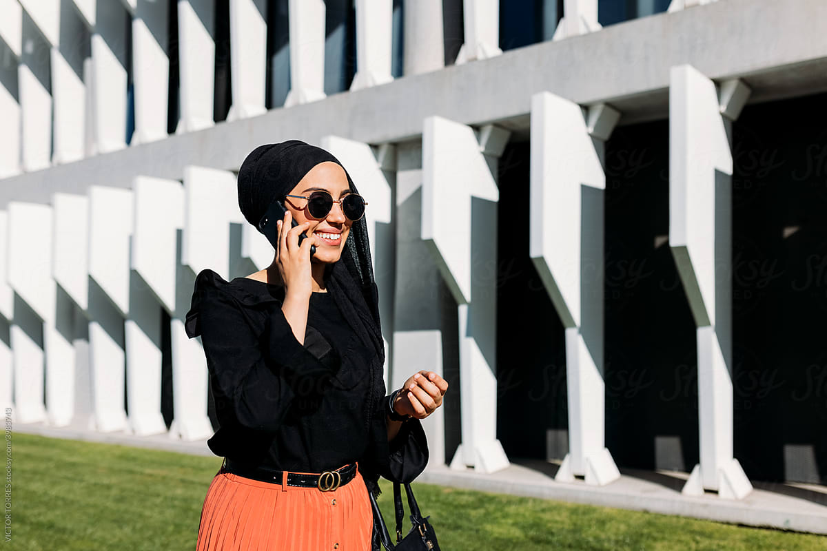 Elegant Muslim woman in stylish outfit speaking on phone on street