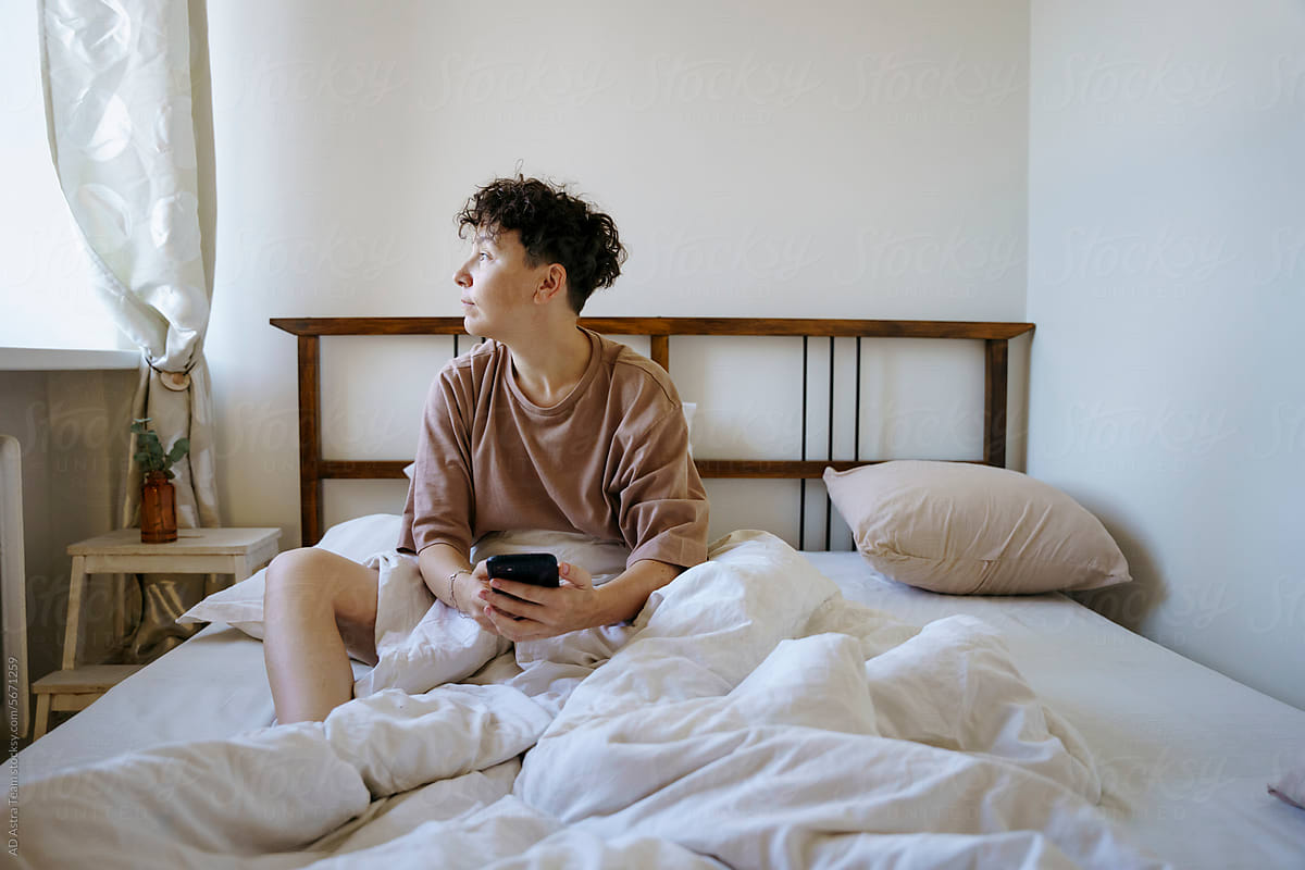 A woman has woken up and is holding a smartphone in her hands