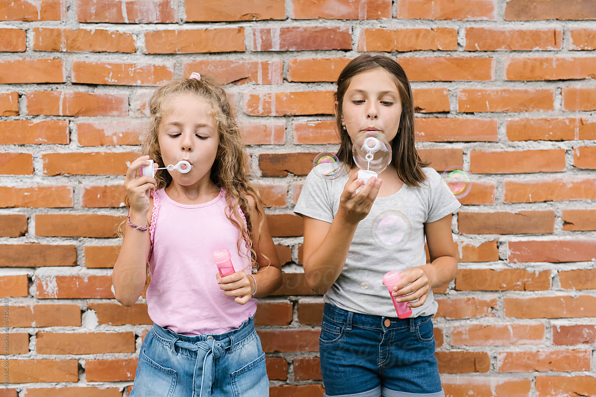 Girls blowing soap bubbles in front of brick wall