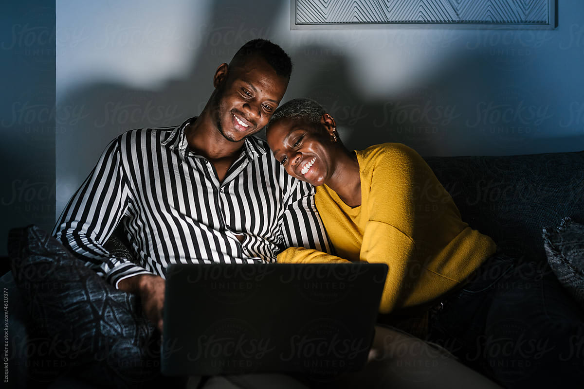 Cheerful black couple chilling on laptop at night