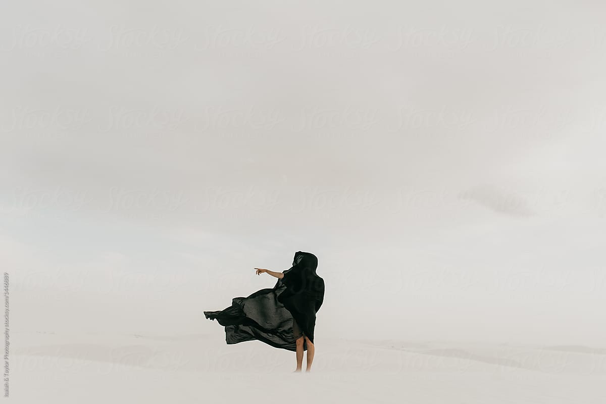 Dark mysterious black cloth blowing in the wind in the desolate desert hiding a human silhouette