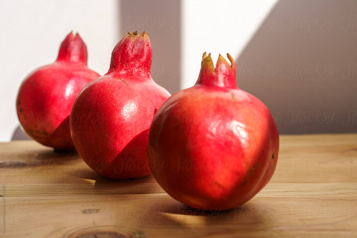 Three Red Pomegranates Fruits on Wooden Table, Sunny Wall Background.