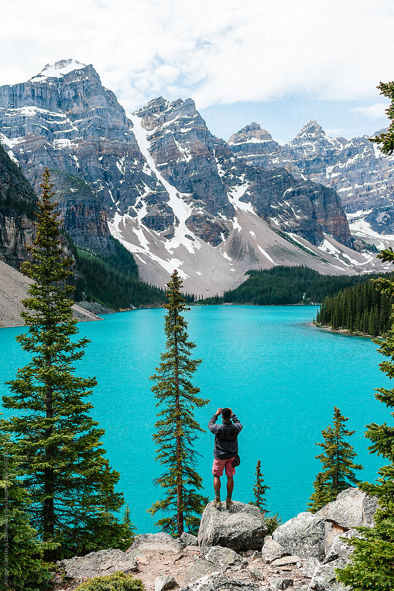 A man standing on a rock taking a photo of Moraine Lake & the mountains