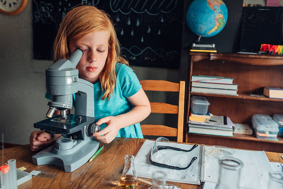 Red haired girl looking through a microscope