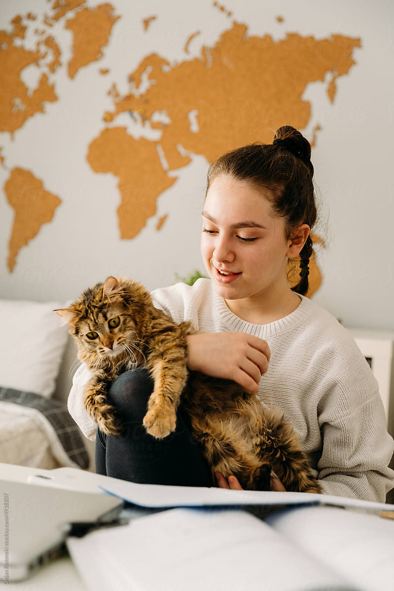 Teenager playing with her cat while studying