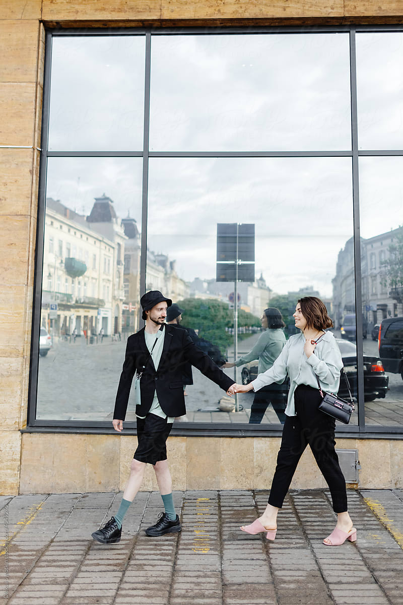Couple in trendy clothes strolling against building with large mirror