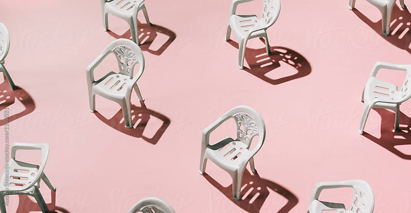 Group of white chairs on pink background.