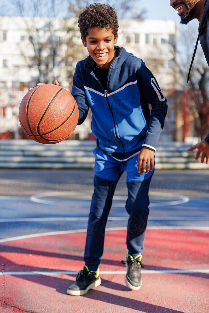 Happy boy dribbling basketball while playing with father on court