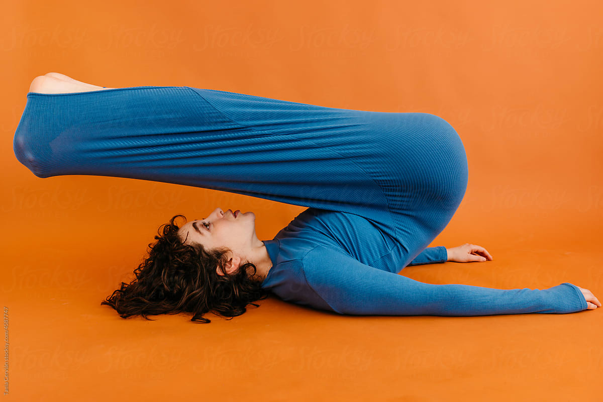 Young lady doing Plow yoga asana in orange studio