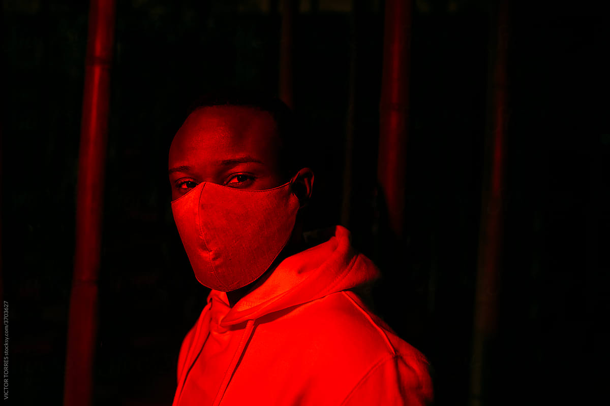 Black man in mask in room with red illumination