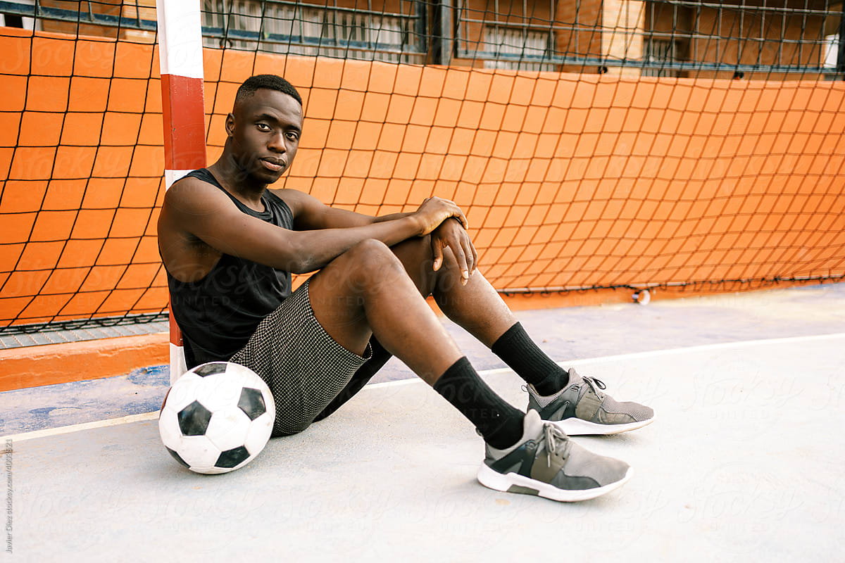Black sportsman sitting near football ball